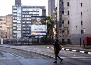 JOHANNESBURG, SOUTH AFRICA - NOVEMBER 8: A homeless man walks past a billboard promoting the upcoming G20 Leaders's Summit stands among housing projects on November 8, 2025 in Braamfontein in central Johannesburg, South Africa. The 2025 G20 Johannesburg summit is the upcoming twentieth meeting of the Group of Twenty heads of state and government planned from 22 to 23 November 2025. (Photo by Per-Anders Pettersson/Getty Images)
