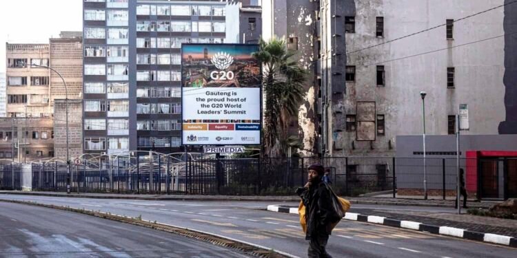 JOHANNESBURG, SOUTH AFRICA - NOVEMBER 8: A homeless man walks past a billboard promoting the upcoming G20 Leaders's Summit stands among housing projects on November 8, 2025 in Braamfontein in central Johannesburg, South Africa. The 2025 G20 Johannesburg summit is the upcoming twentieth meeting of the Group of Twenty heads of state and government planned from 22 to 23 November 2025. (Photo by Per-Anders Pettersson/Getty Images)